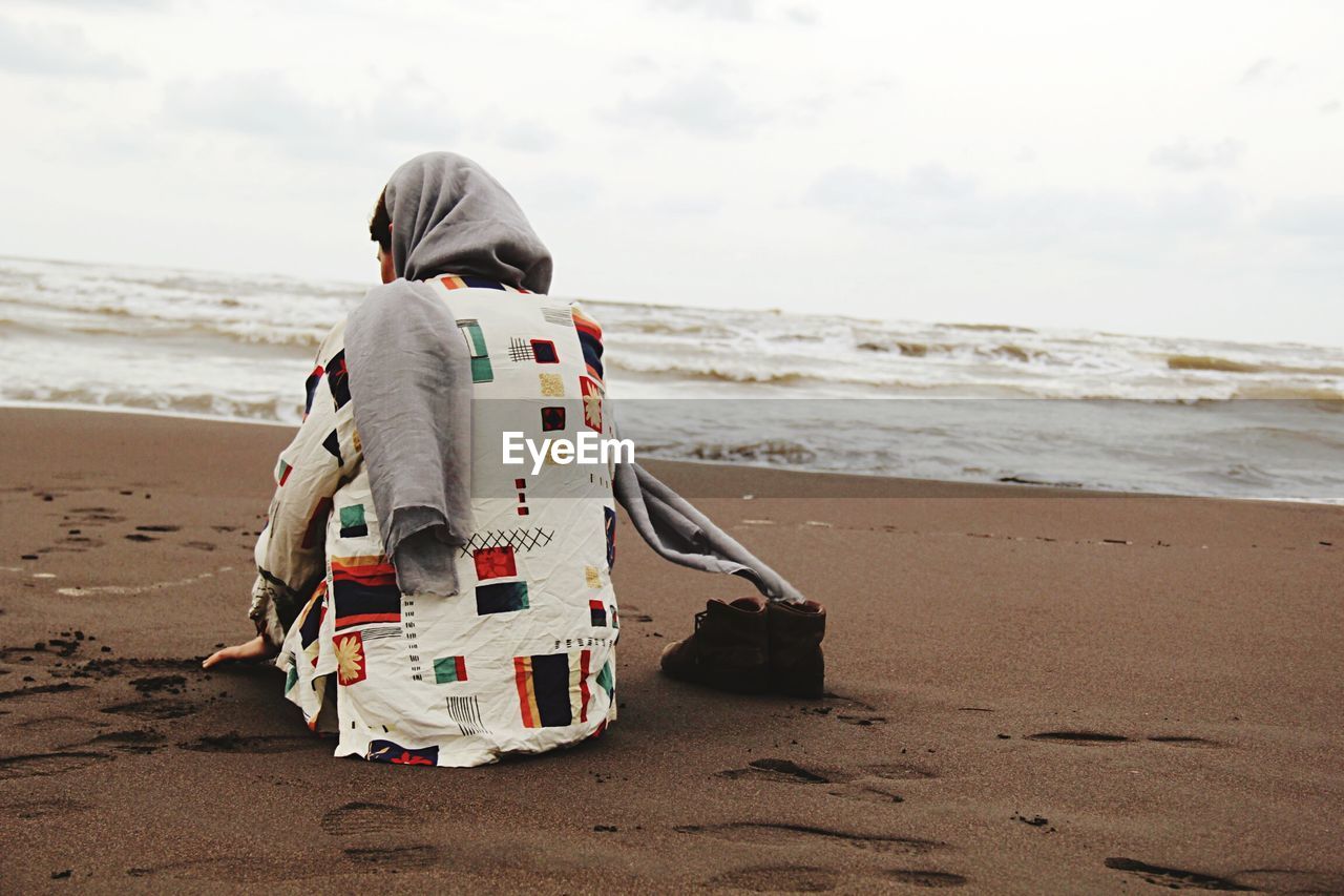 Woman sitting at sandy beach against sky