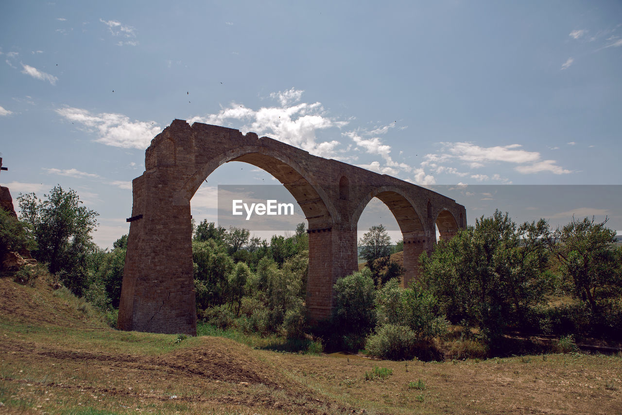 High ruined stone bridge stands in the summer in a field above the river in russia