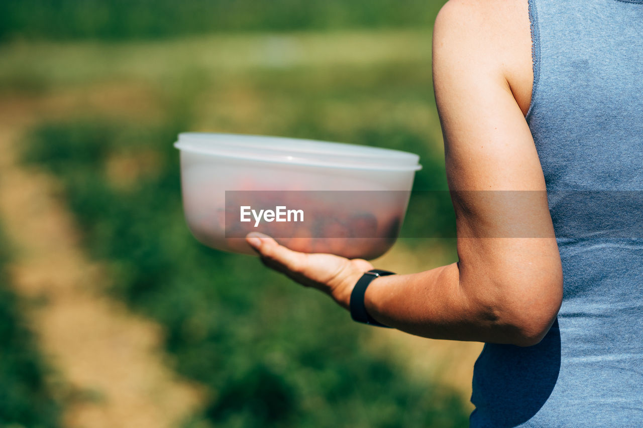 Cropped image of woman holding strawberries in container on field