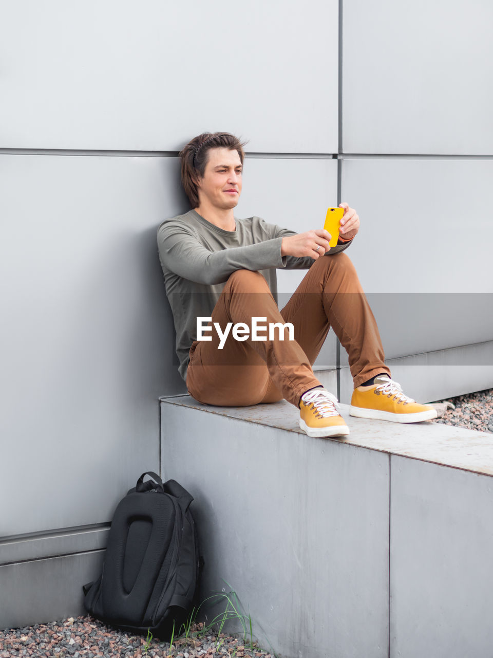 Thoughtful young man sits with smartphone. student with rucksack in casual clothes. 