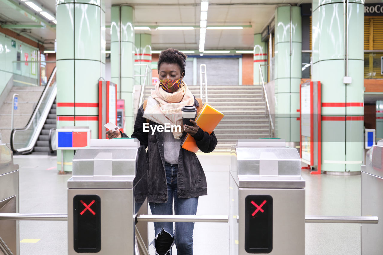 University female african student wearing protective face mask passing through the turnstiles with her transport card at the underground station. new normal in public transport.