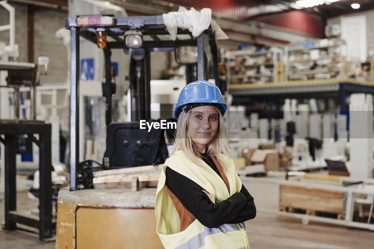 Confident engineer standing with arms crossed in factory