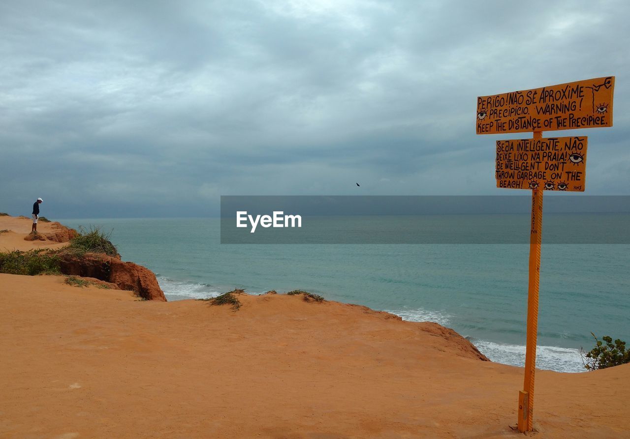 Signboard on cliff by sea against cloudy sky