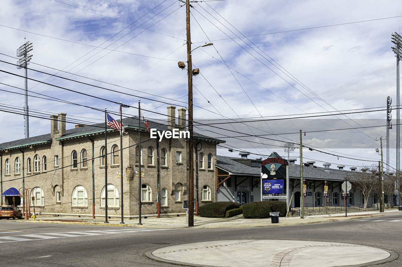 architecture, cable, transportation, transport, electricity, built structure, city, building exterior, residential area, sky, road, street, urban area, power line, cloud, neighbourhood, town, downtown, technology, mode of transportation, day, nature, sign, vehicle, electricity pylon, infrastructure, suburb, power supply, building, outdoors, no people, city street, travel destinations, lane, power generation, communication