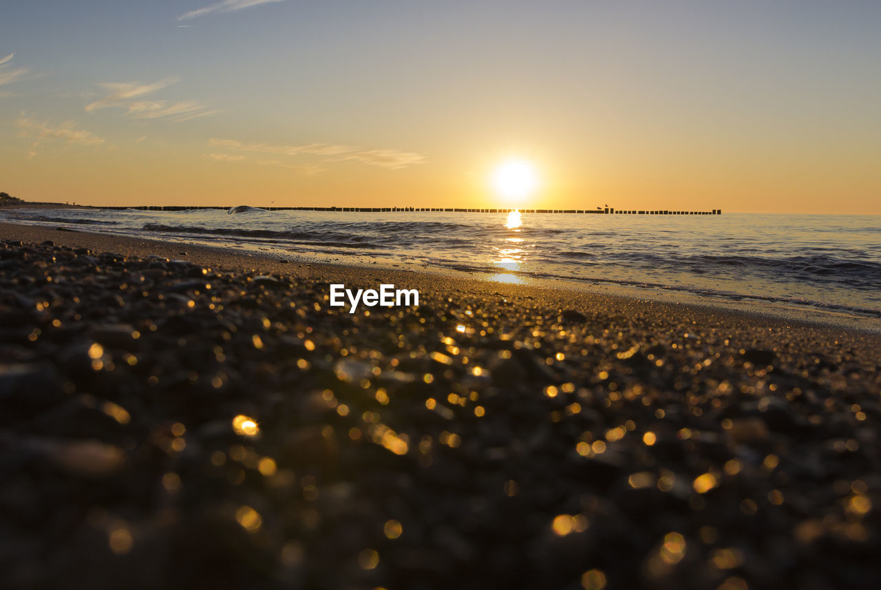 SURFACE LEVEL OF BEACH AGAINST SKY DURING SUNSET