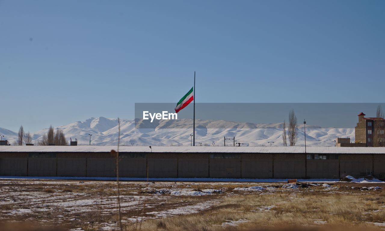 Iranian flag on field against mountain range clear sky during winter with snow