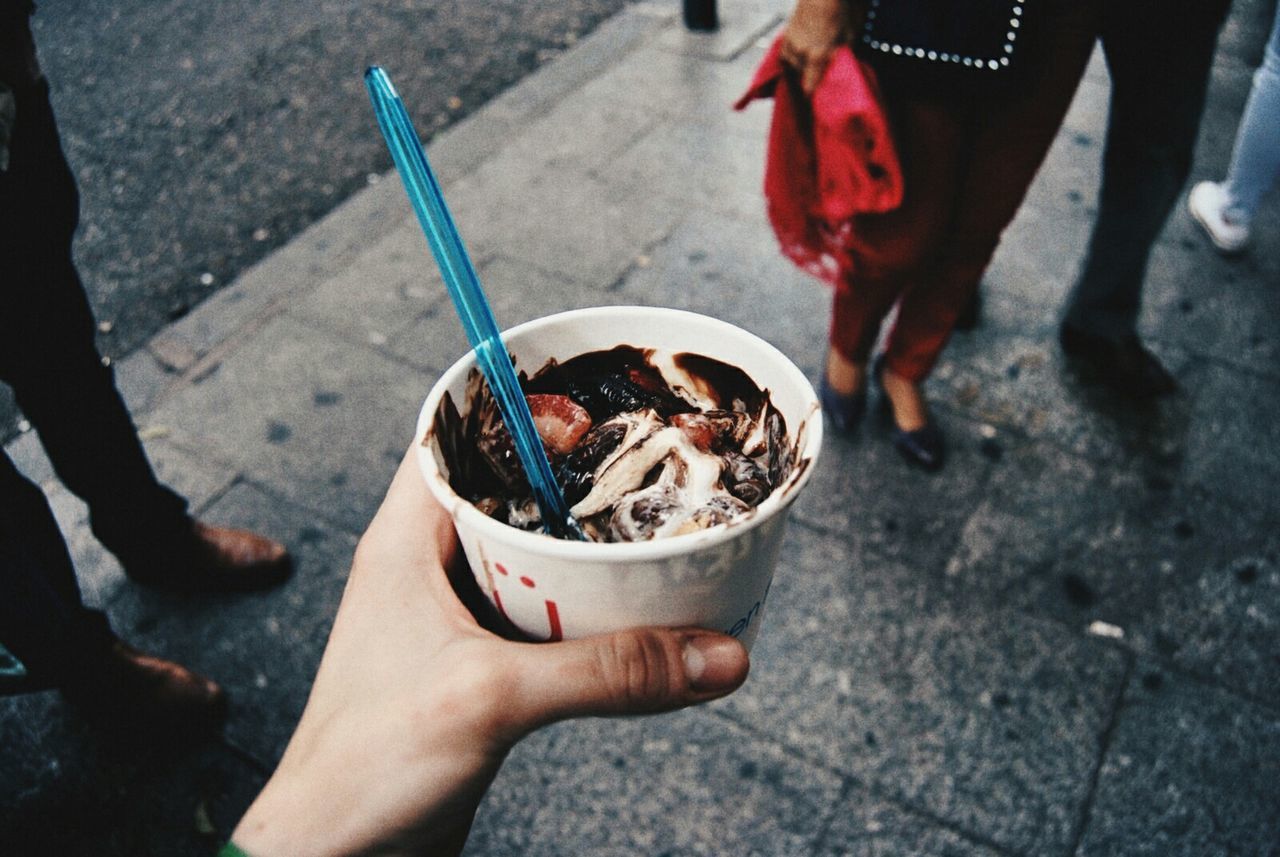 Cropped image of hand holding frozen yoghurt in disposable cup at city