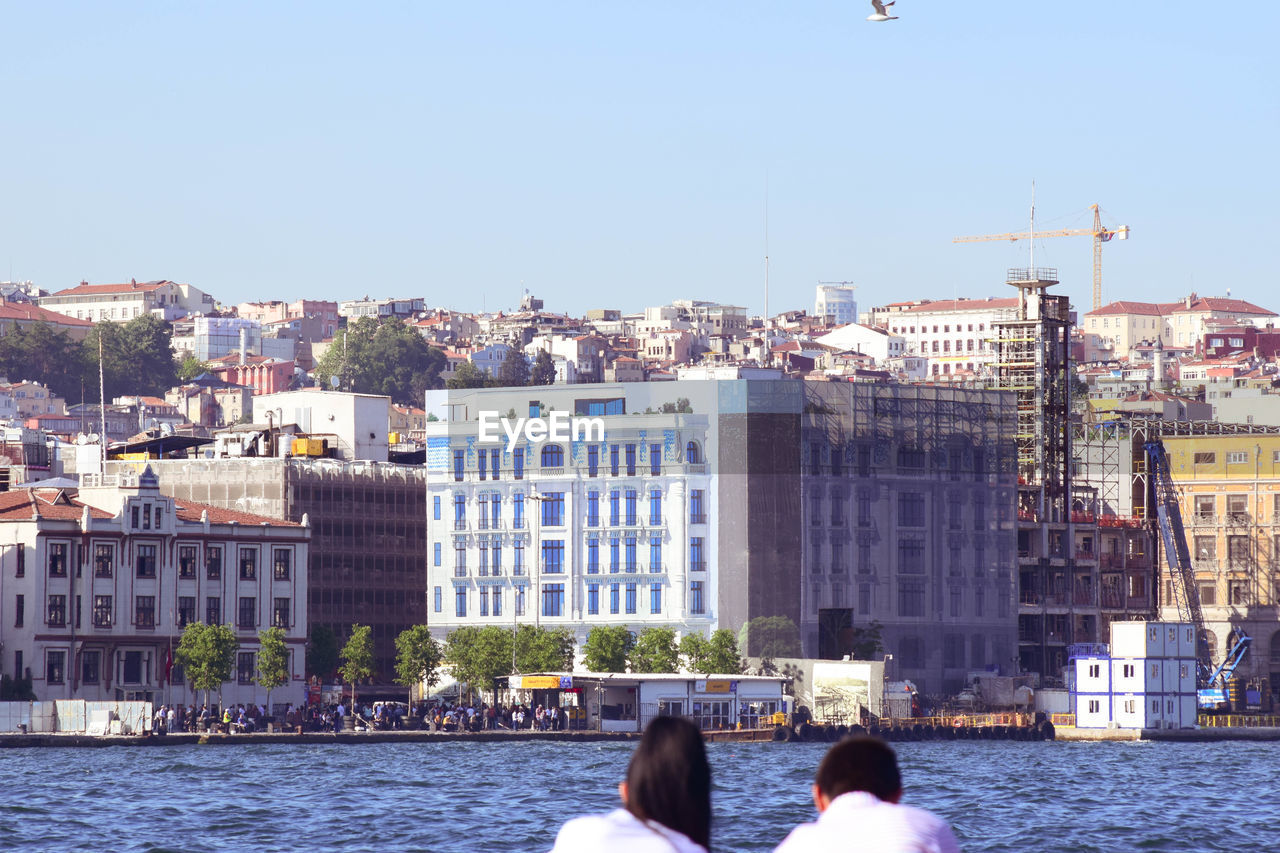 REAR VIEW OF PEOPLE ON RIVER AMIDST BUILDINGS IN CITY