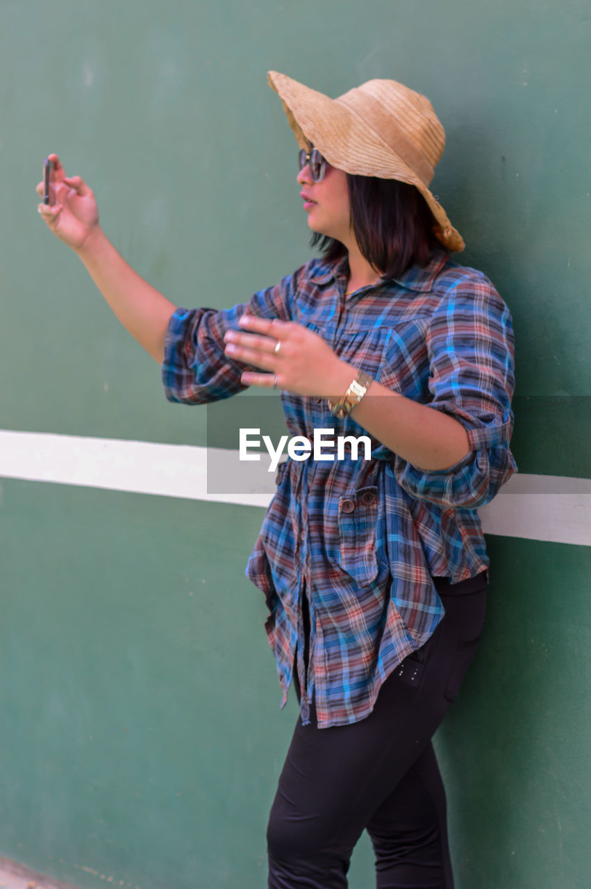 Woman wearing hat while taking selfie against wall
