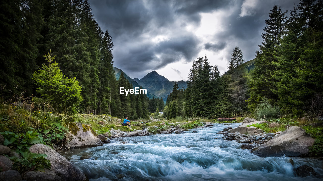 Flowing river and trees against cloudy sky