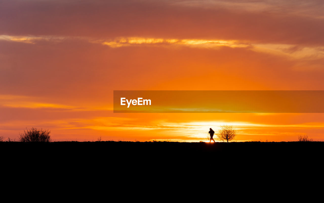 SILHOUETTE PEOPLE ON FIELD AGAINST ORANGE SKY