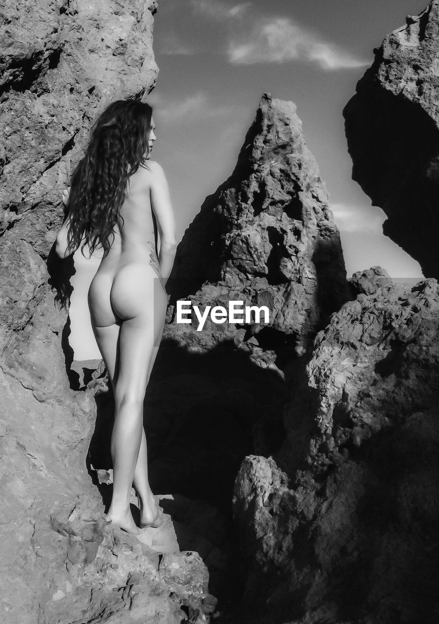 Rear view of naked woman standing on rock formation