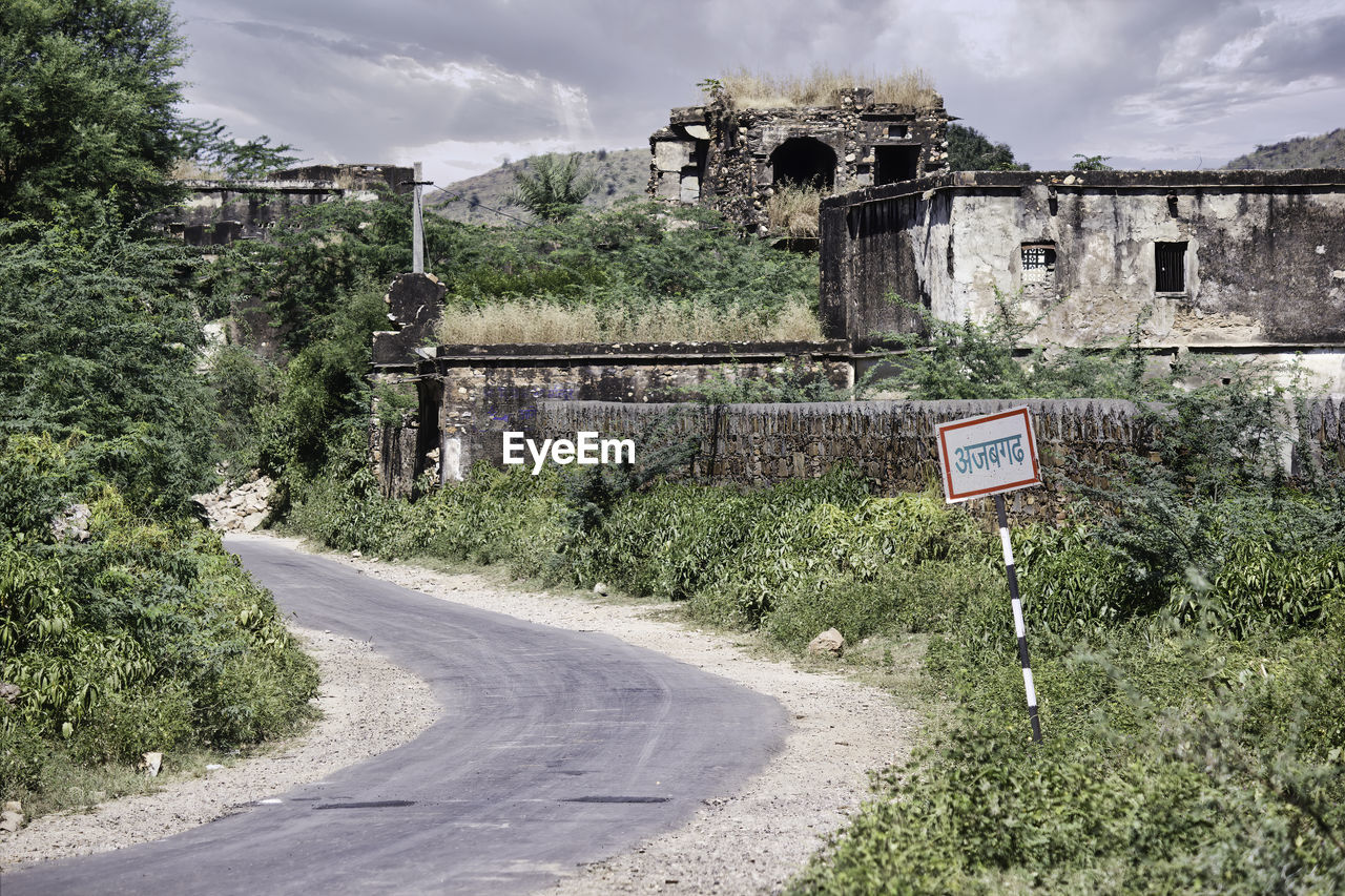 Road sign by trees against sky in city in bhangarh fort, rajasthan 