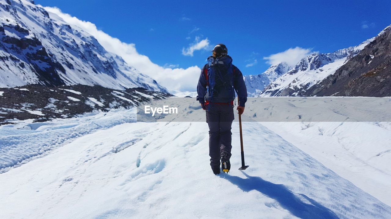 REAR VIEW OF MAN ON SNOWCAPPED MOUNTAIN