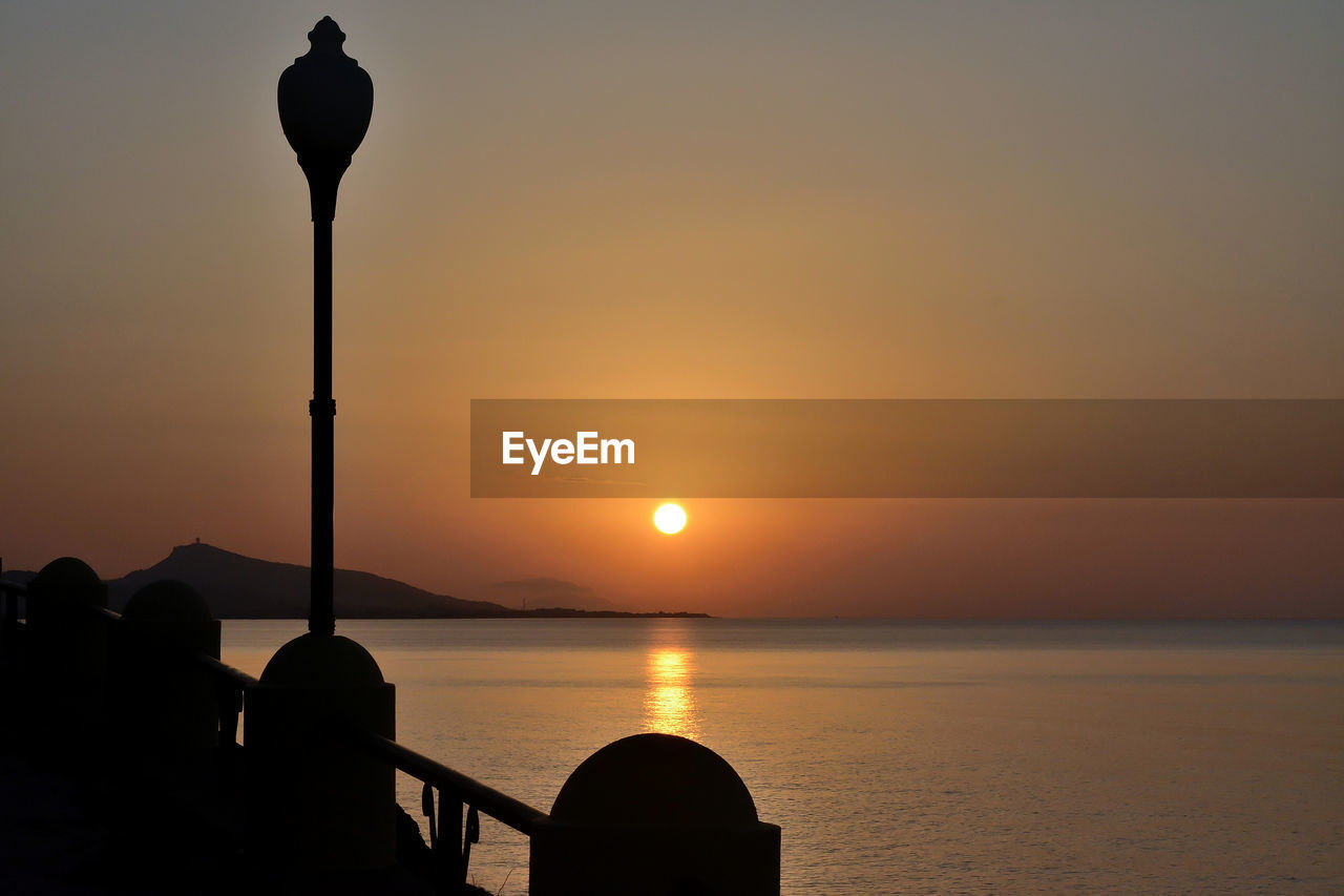 Silhouette street light by sea against sky during sunset