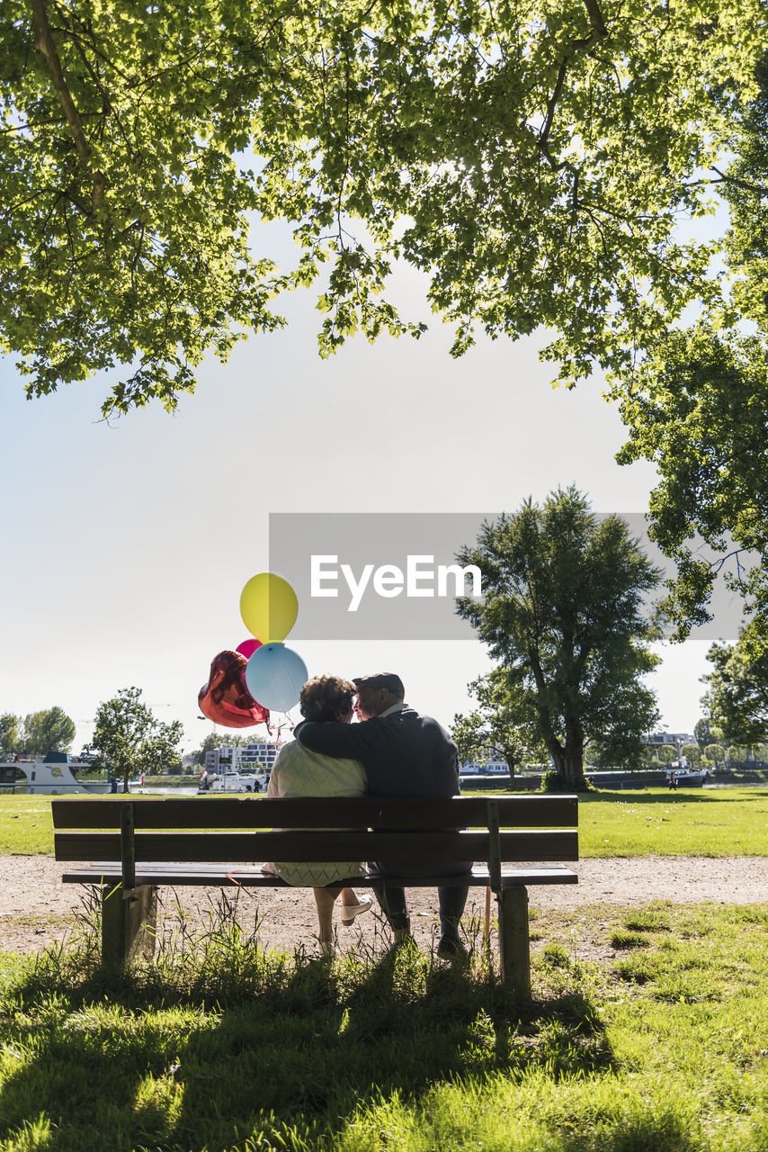 Happy senior couple with balloons kissing on bench in a park