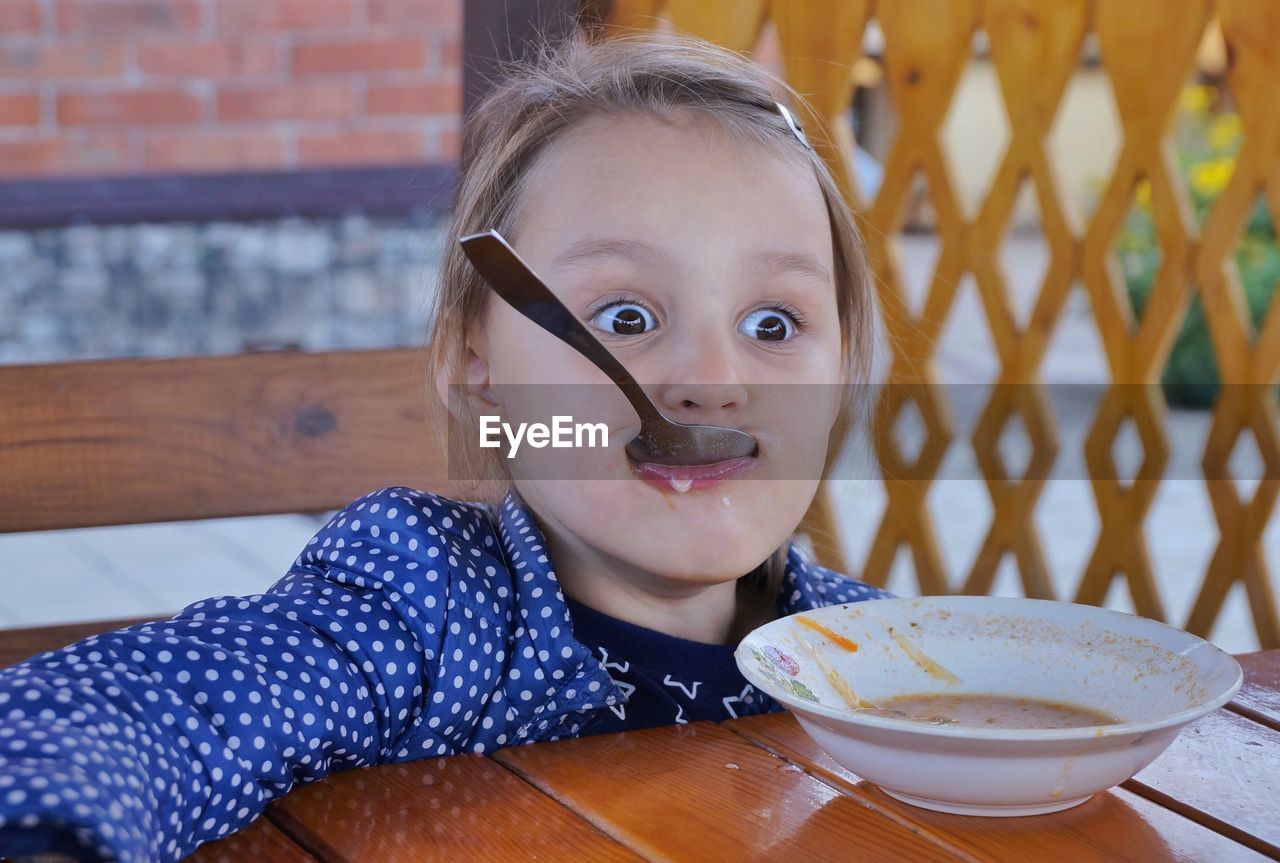 Girl looking away while eating soup on wooden table