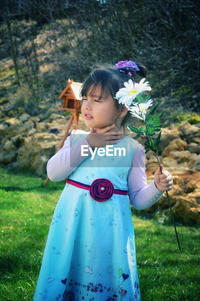 Cute girl touching her neck while holding flowers in yard