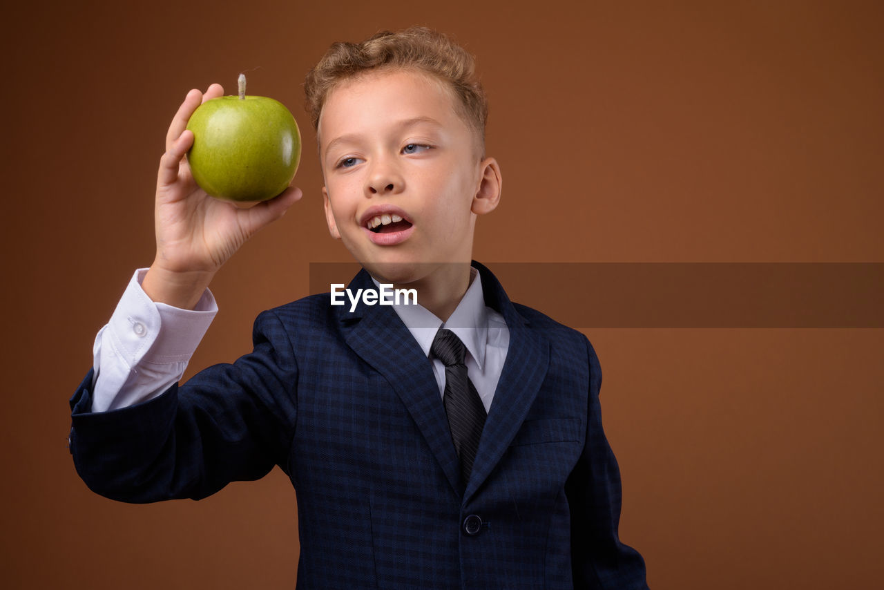 Full length of happy boy holding apple against orange background