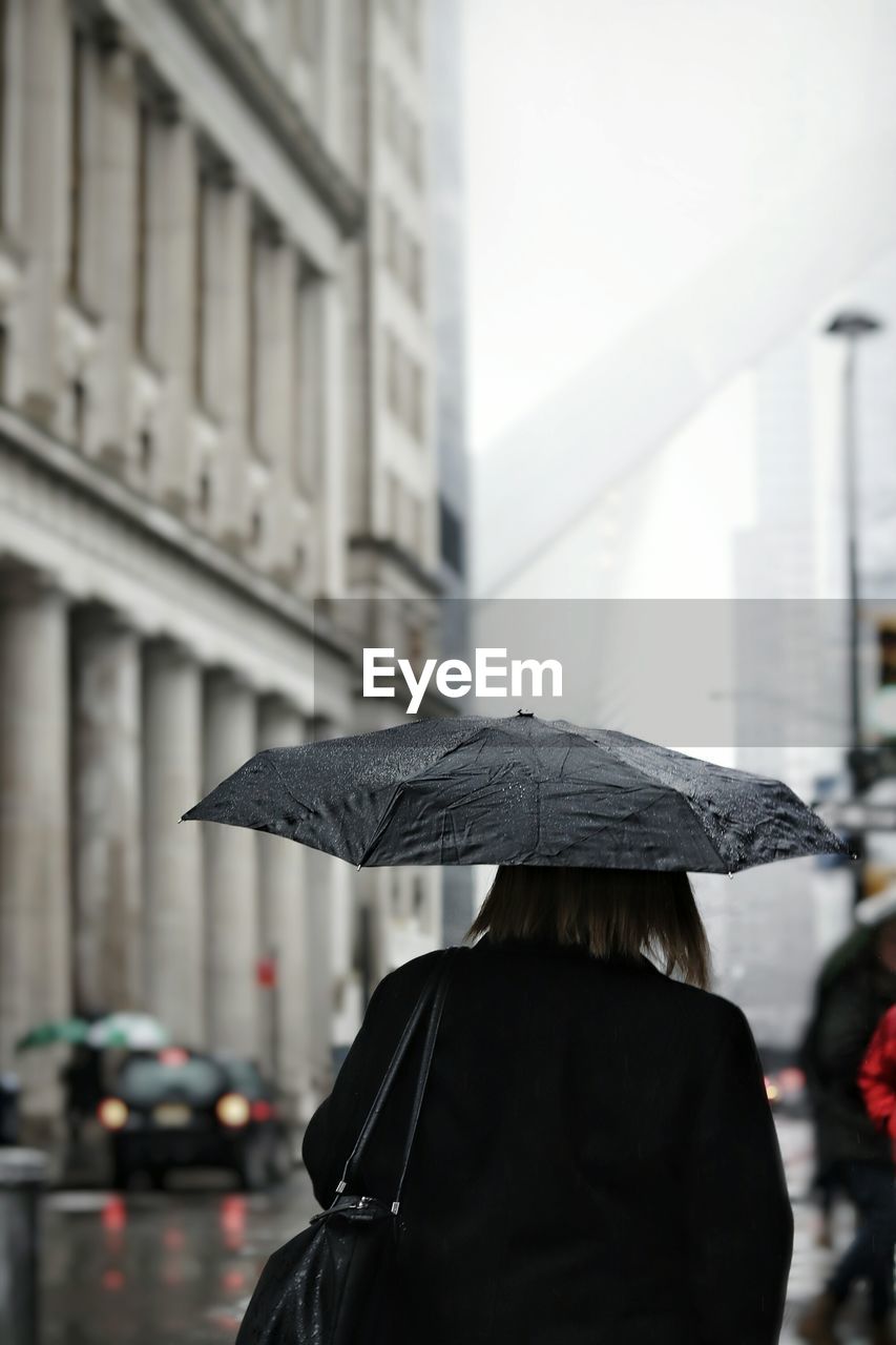 Rear view of woman walking with umbrella on street during rainy season