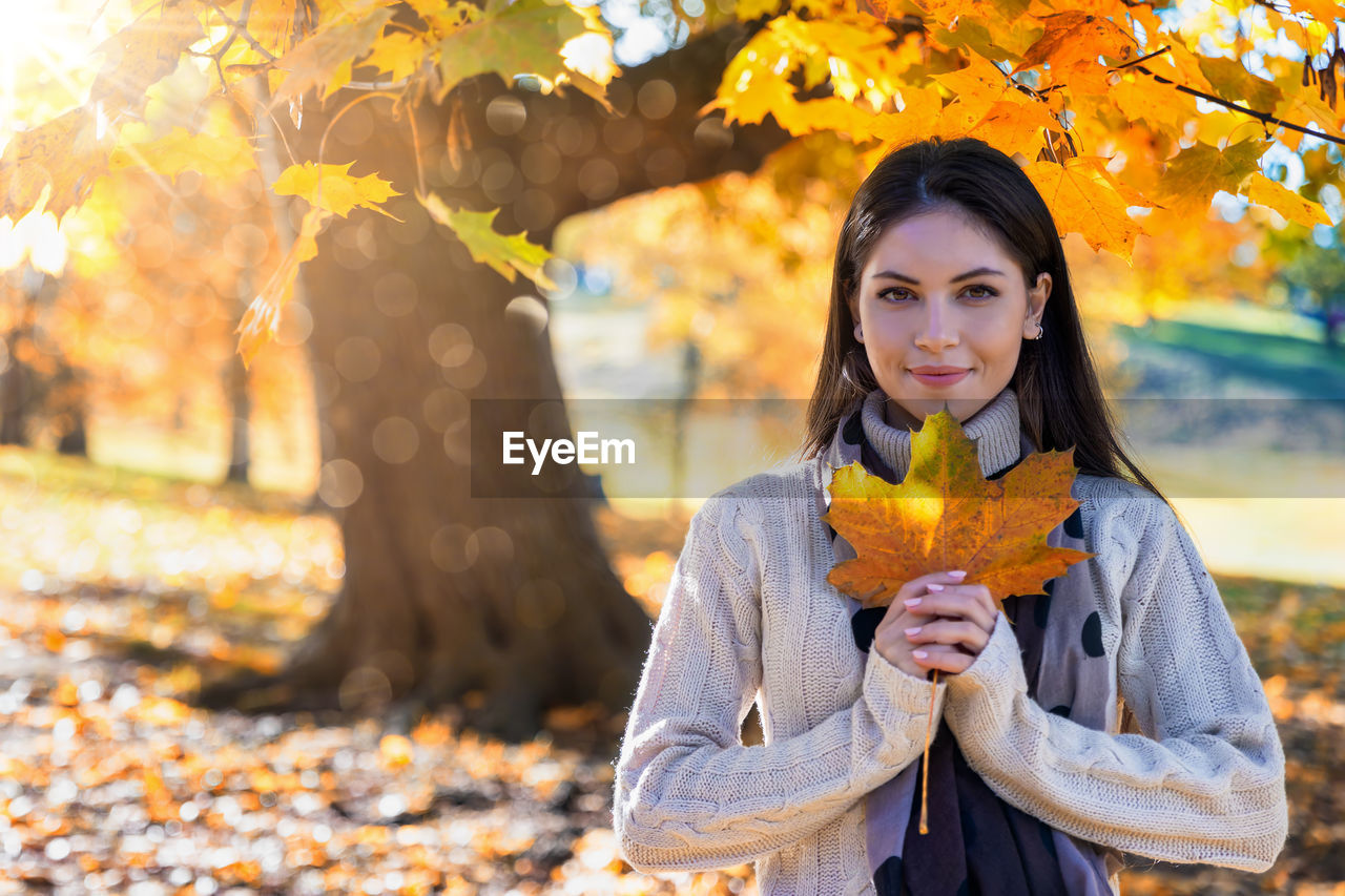 Portrait of young woman holding maple leaf during autumn