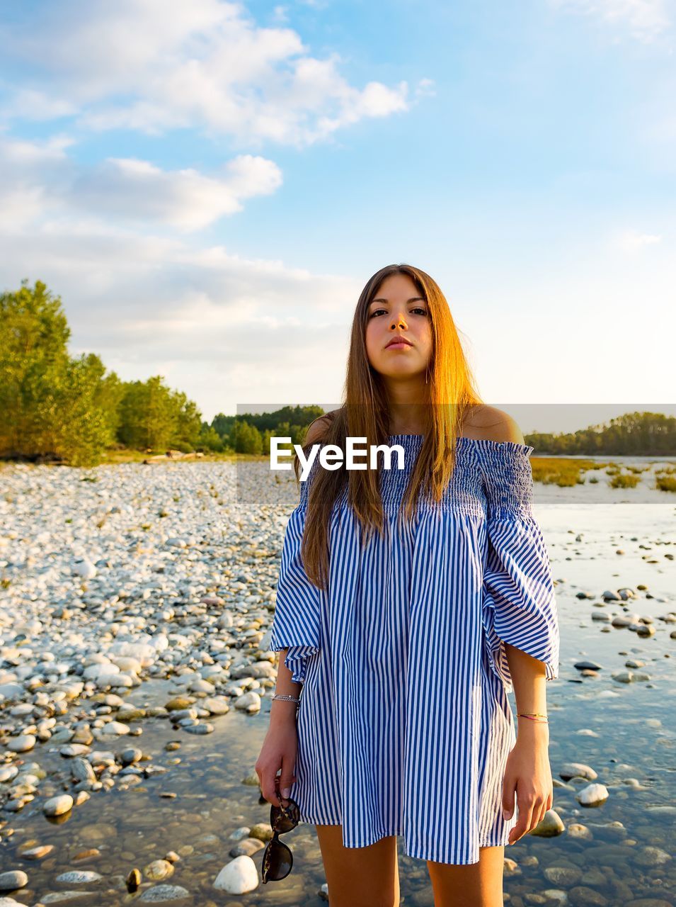 Portrait of beautiful young woman standing against lake