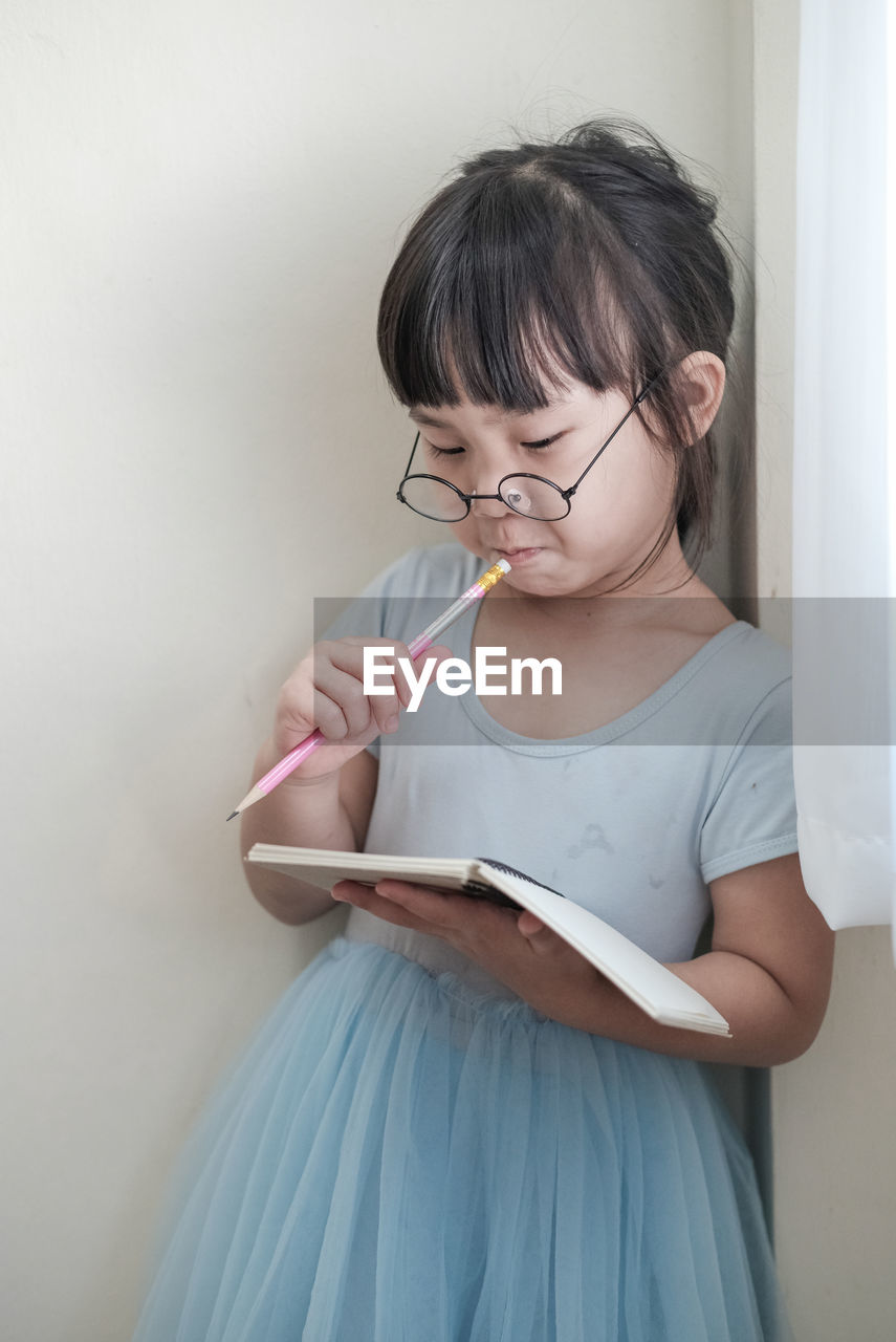 A child with glasses holding a pencil and write in the notebook intently. isolated