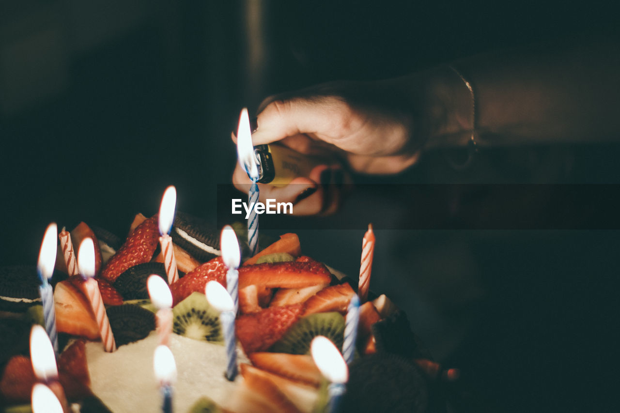 Close-up of woman igniting candles on birthday cake