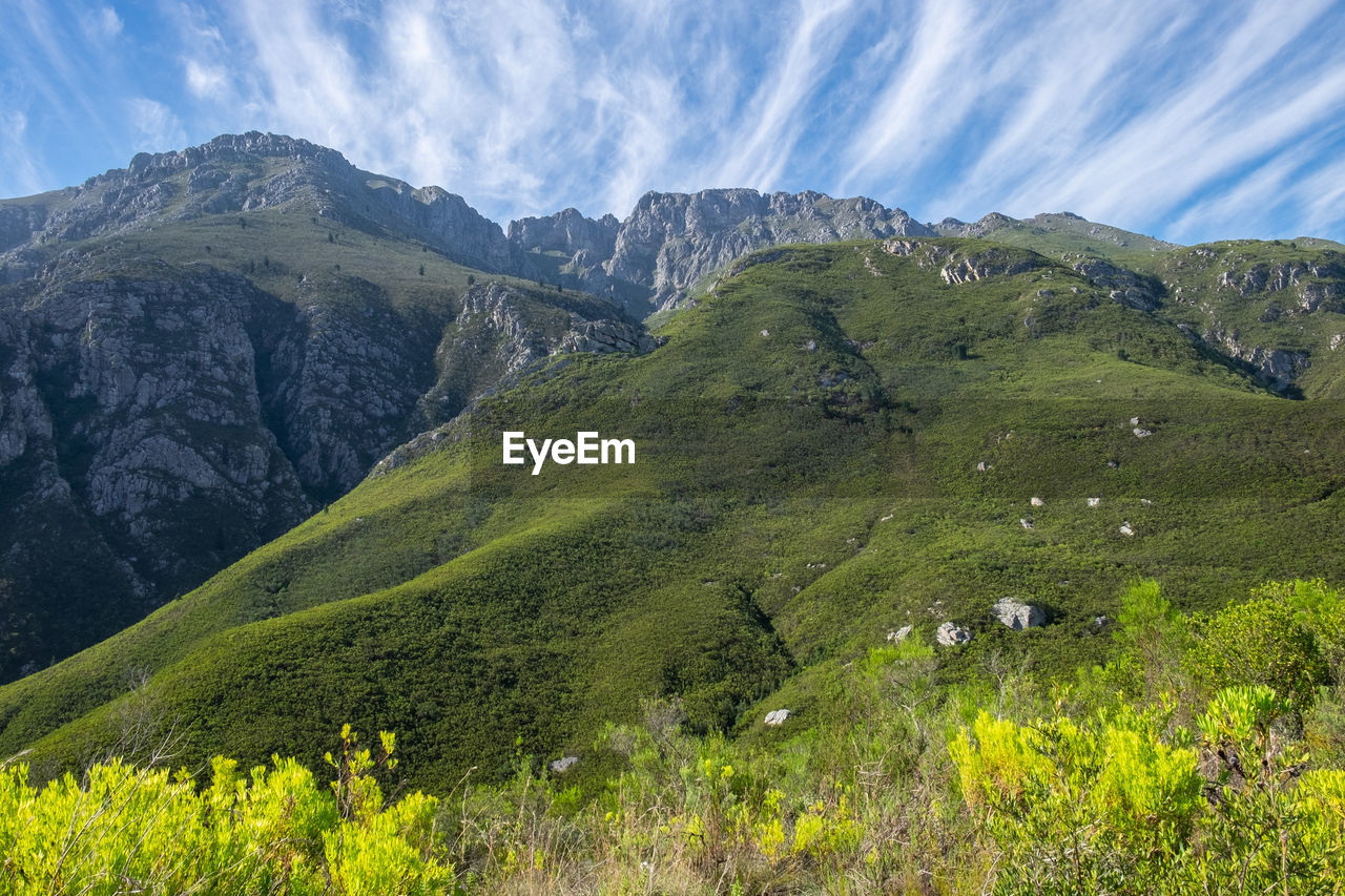 View of green mountain with steaks of clouds above 