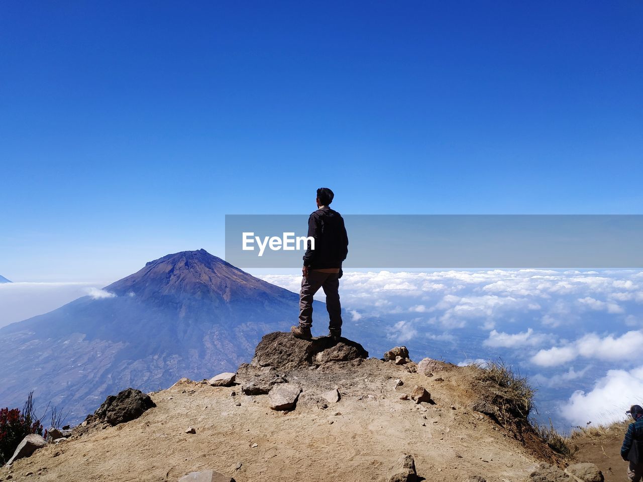 Back view of man alone standing on mountain looking up at blue blue sky