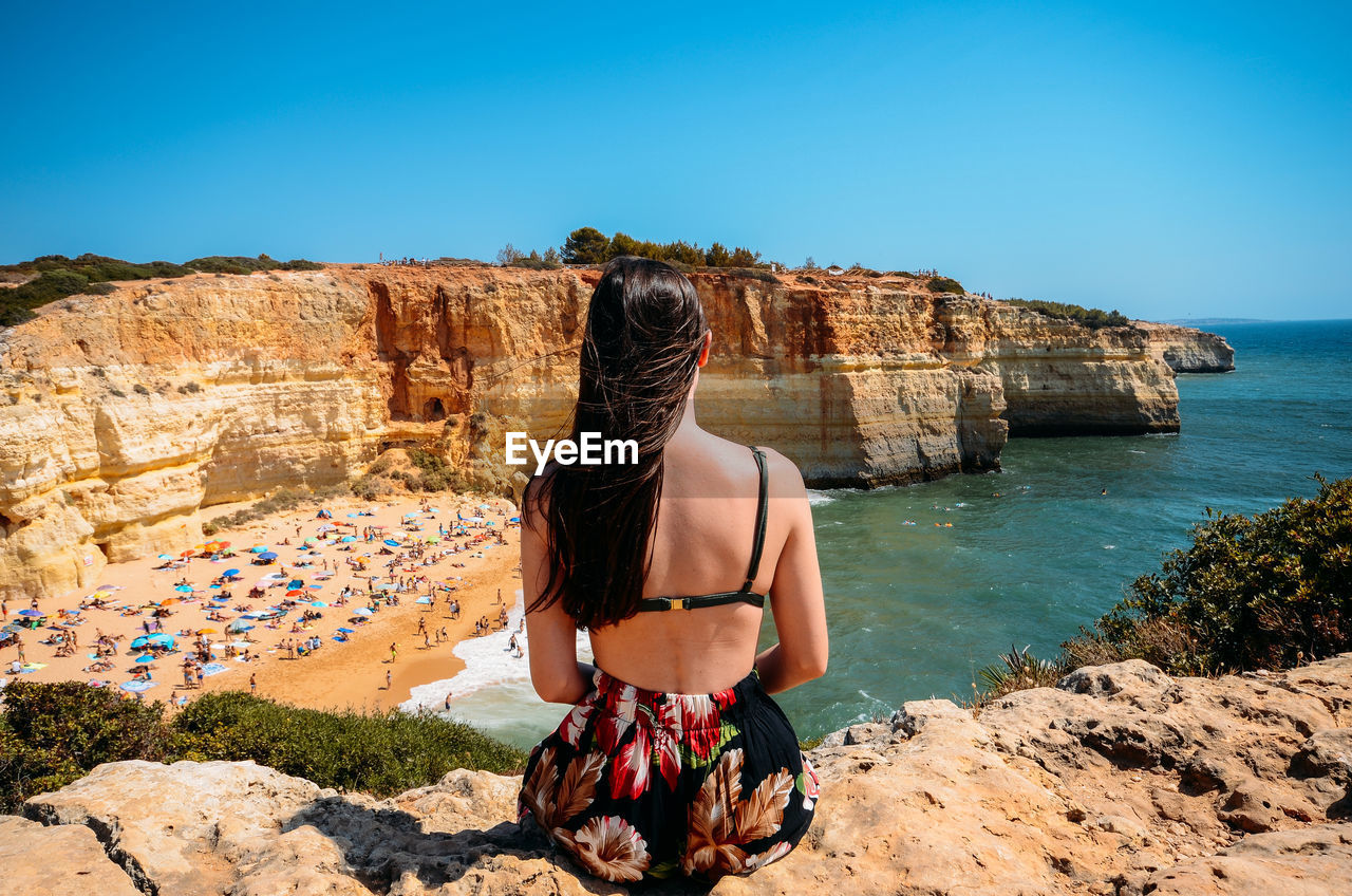 REAR VIEW OF WOMAN LOOKING AT SEA SHORE AGAINST SKY