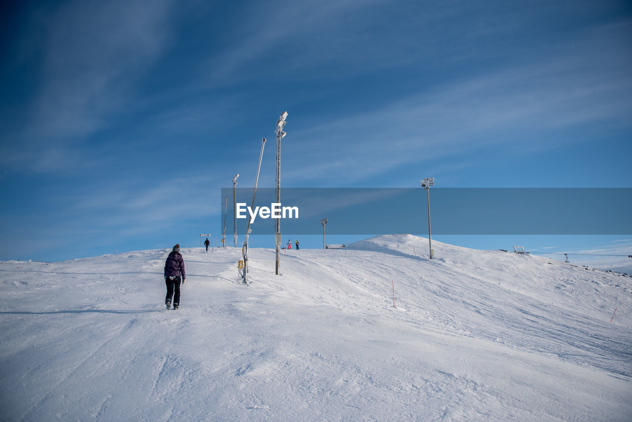 Rear view of person walking on snow covered field against sky