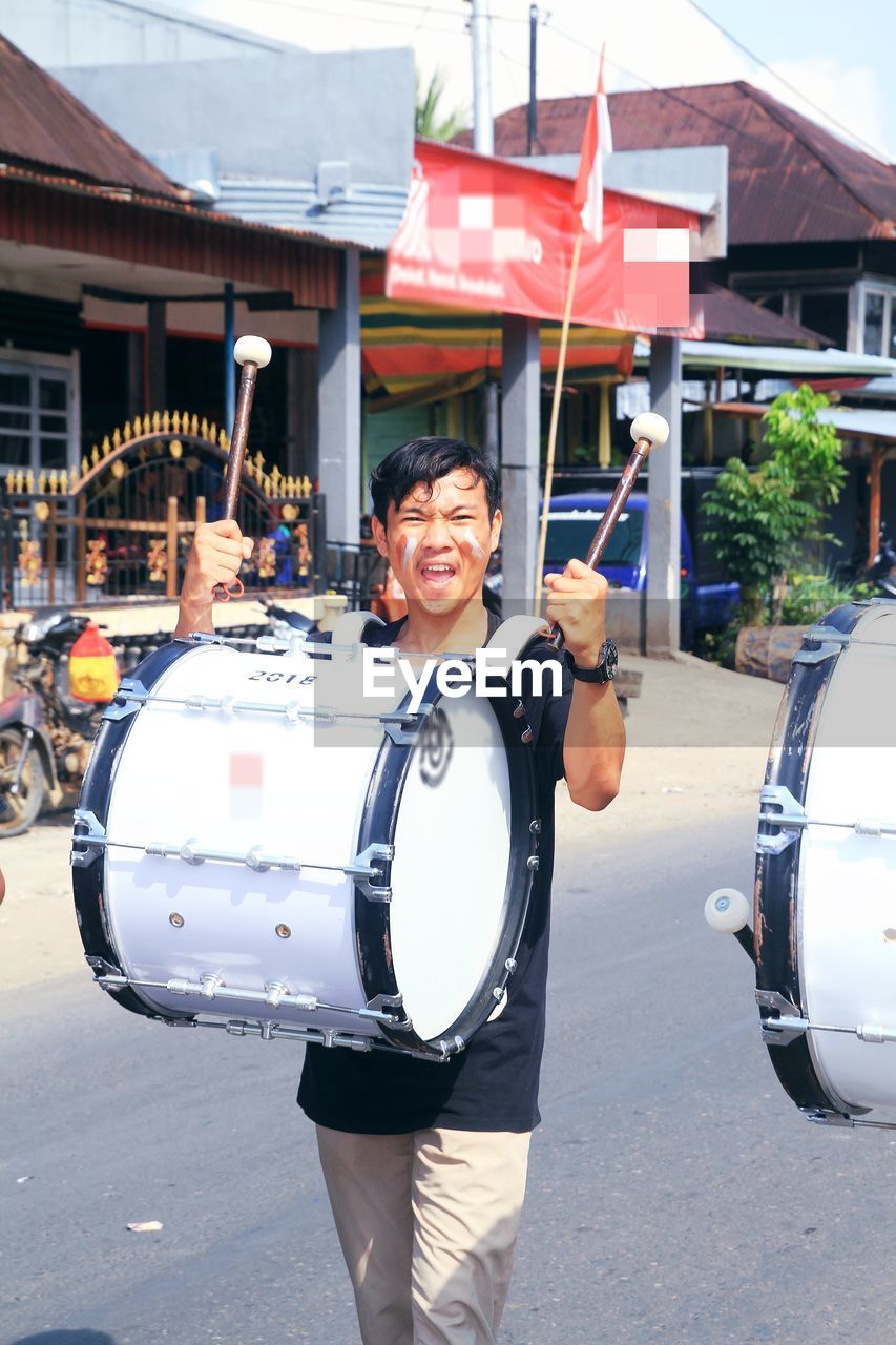 Portrait of smiling man with drum on street in city