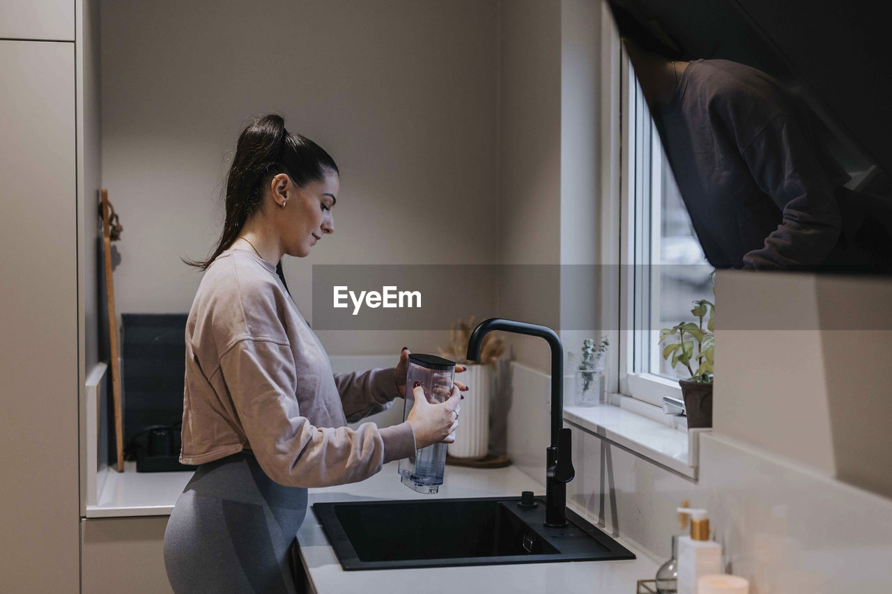 Woman in kitchen filling jug with water