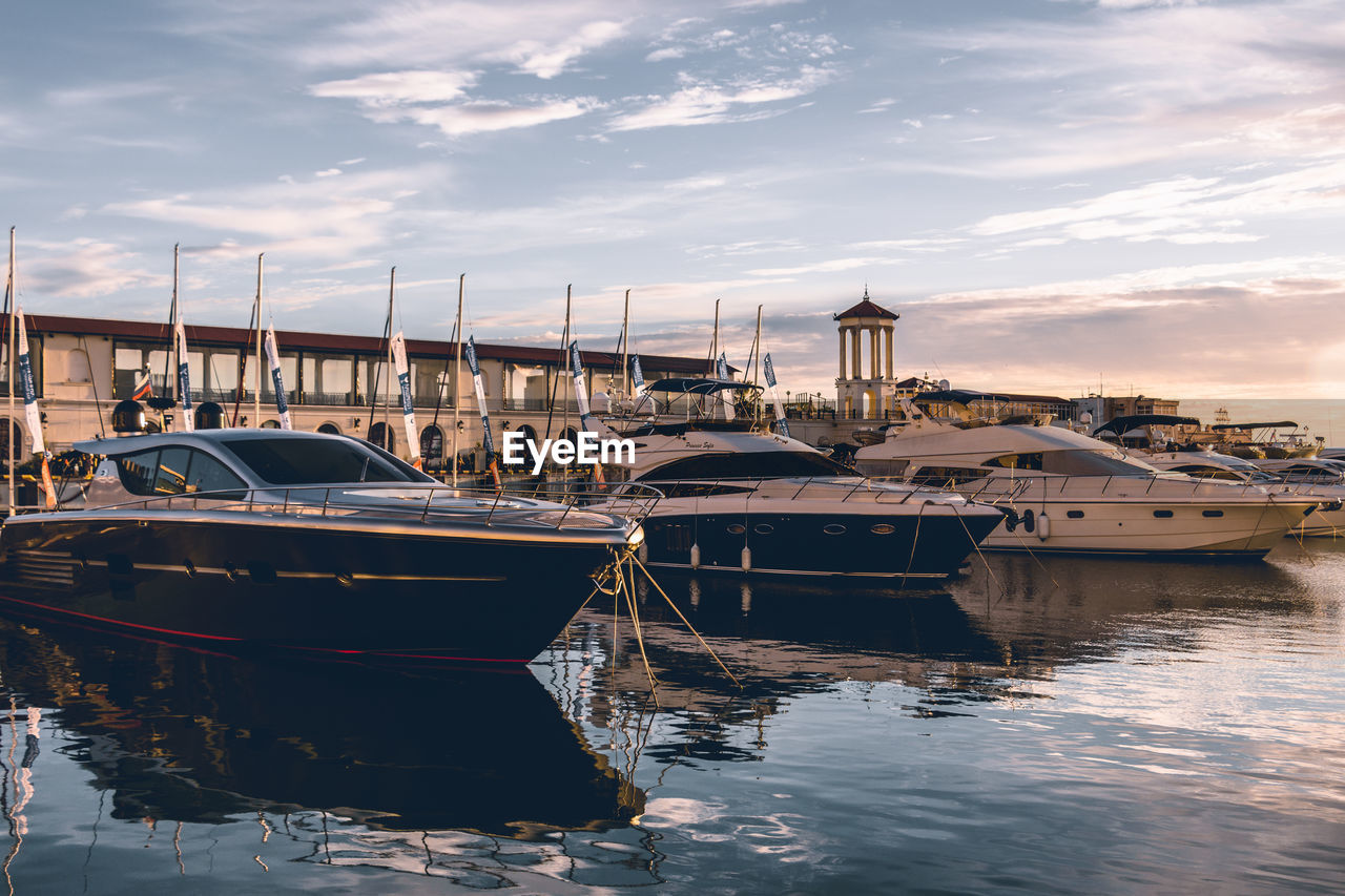 Sailboats moored in harbor at sunset