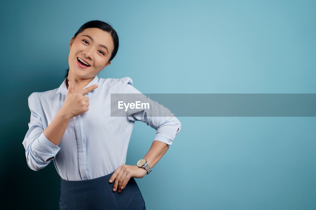 SMILING YOUNG WOMAN AGAINST BLUE BACKGROUND
