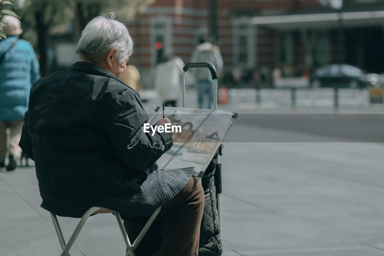 REAR VIEW OF MAN SITTING ON STREET