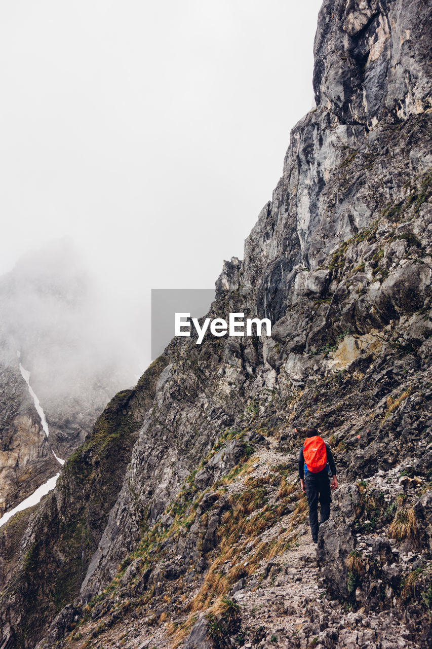 Rear view of hiker with backpack walking on cliff during foggy weather