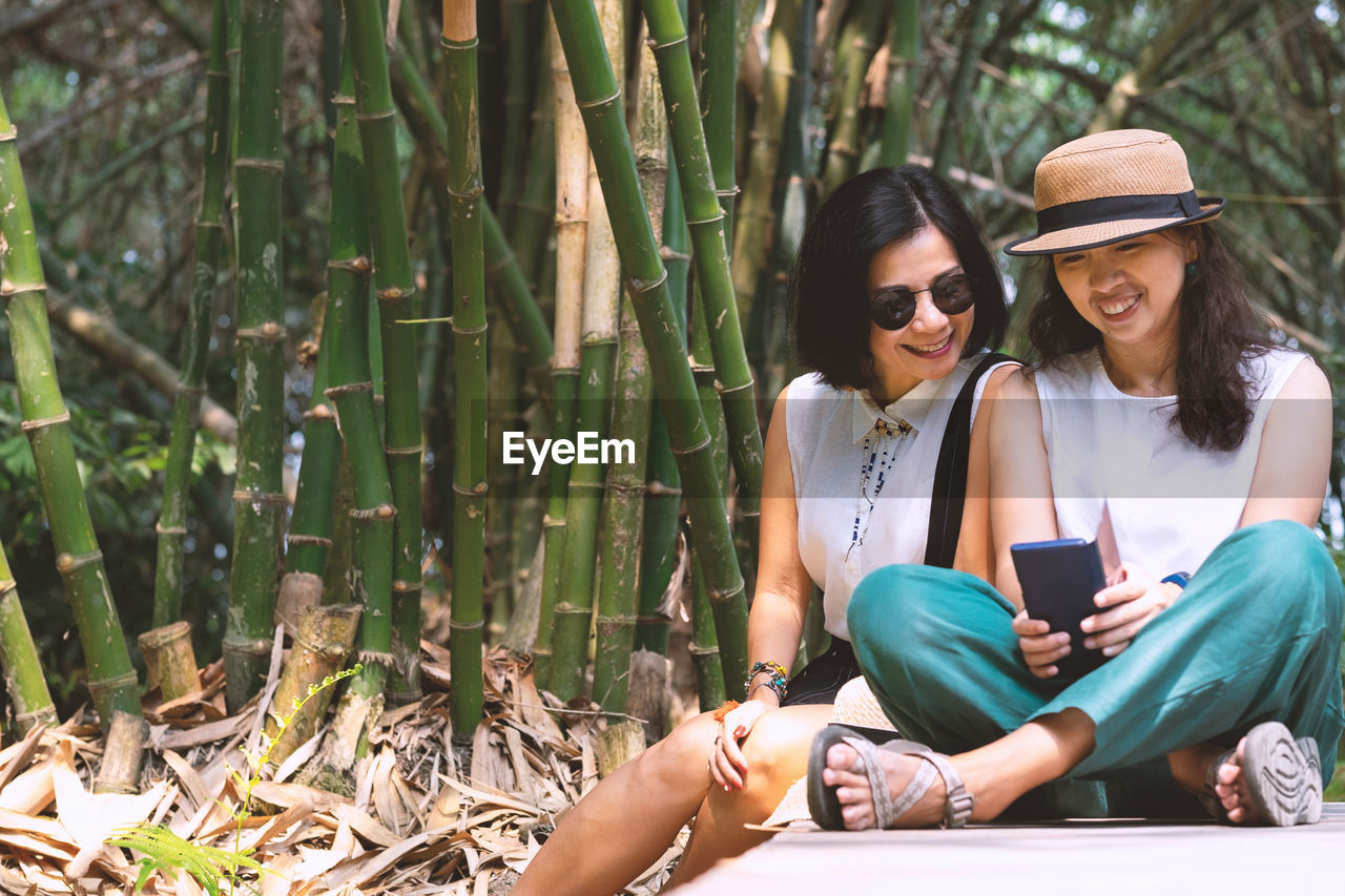 Smiling women looking at mobile phone while sitting by plants