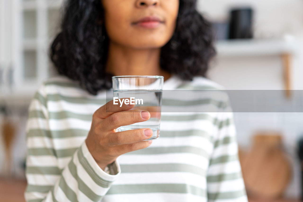 Faceless cropped african-american female drinking glass of water in kitchen. refreshing start of day