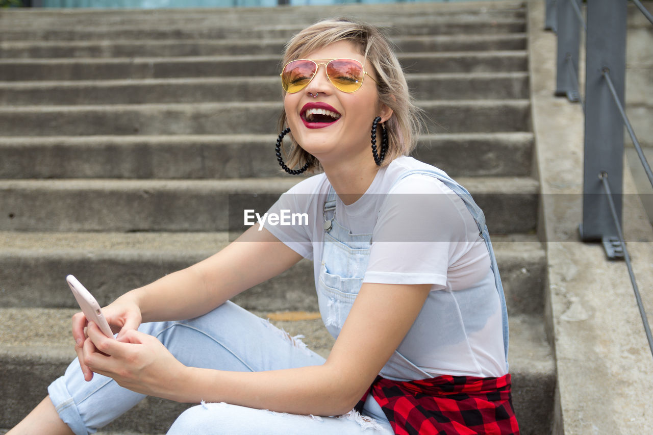 Portrait of smiling woman using mobile phone on steps