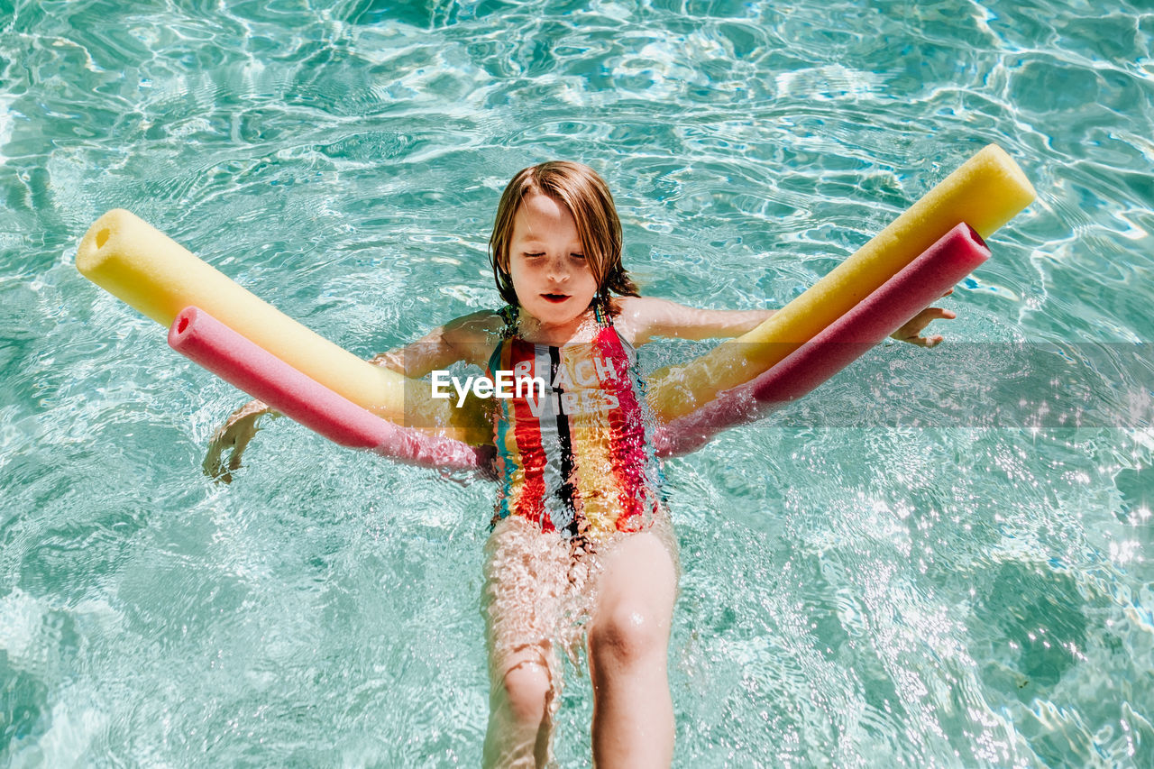 Young girl floating on her back in pool with pool noodles