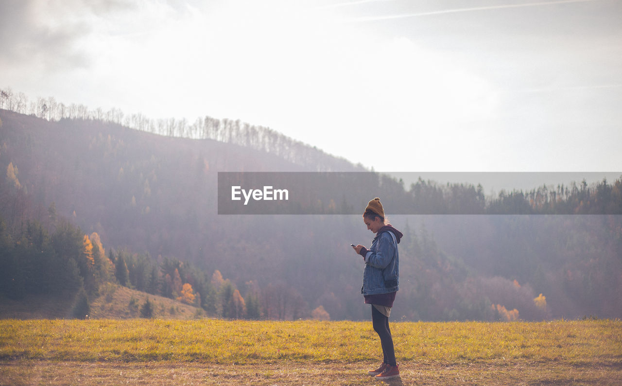 FULL LENGTH OF WOMAN STANDING ON FIELD AGAINST SKY