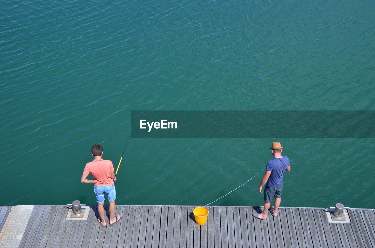 High angle view of men fishing while standing on pier at lake