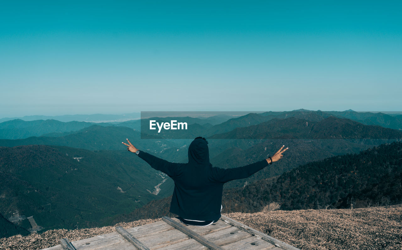 Rear view of man with arms outstretched on mountain against sky