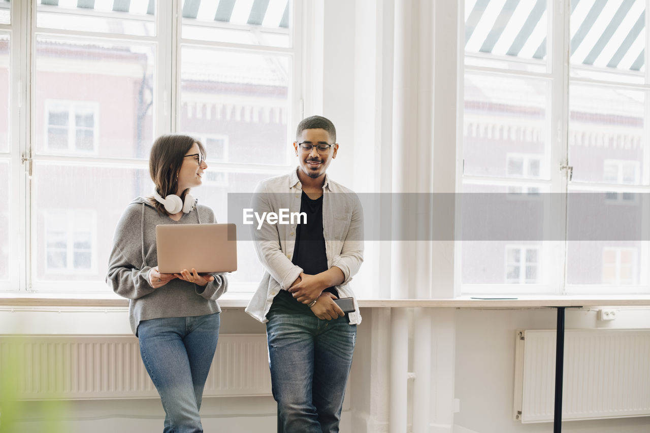 Smiling computer programmers talking while standing by desk in office