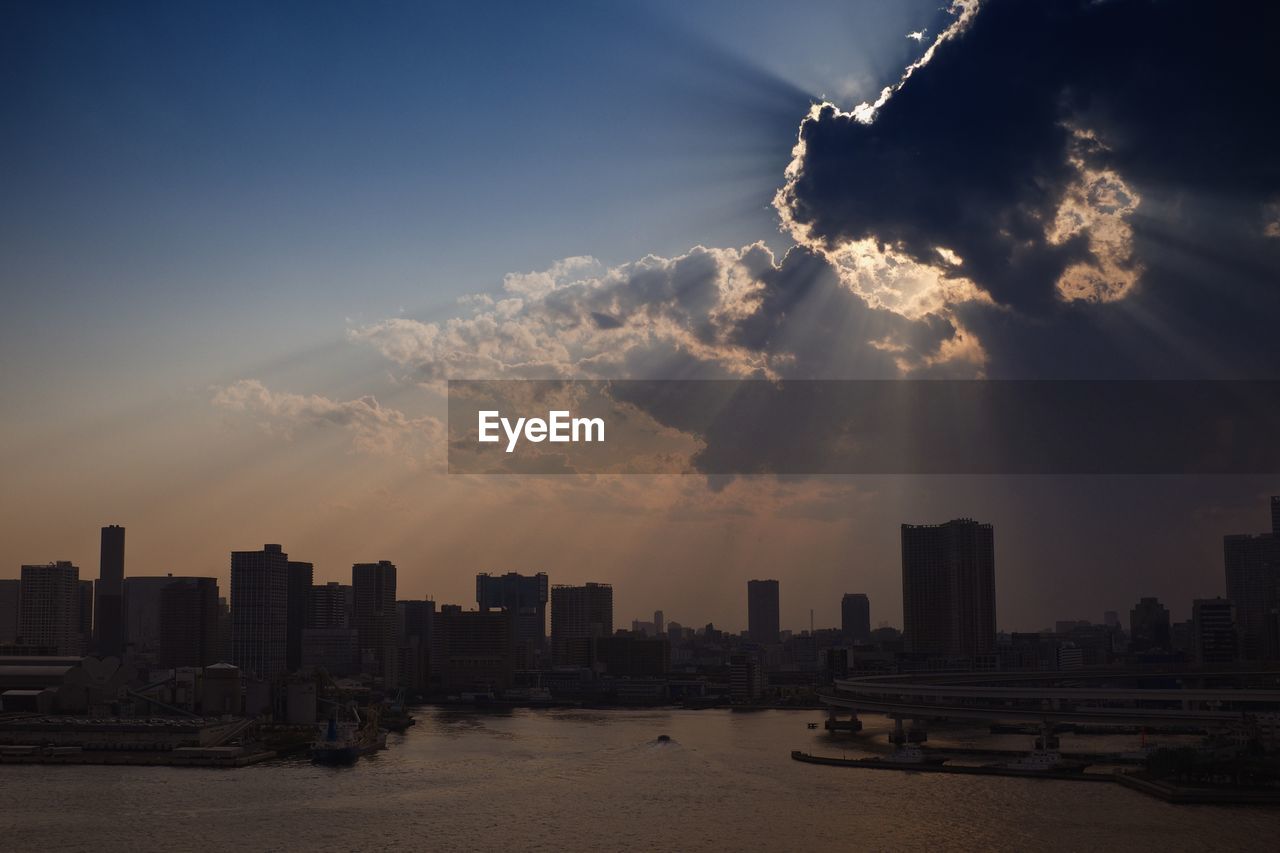 Sunbeam on city and bay against sky during sunset