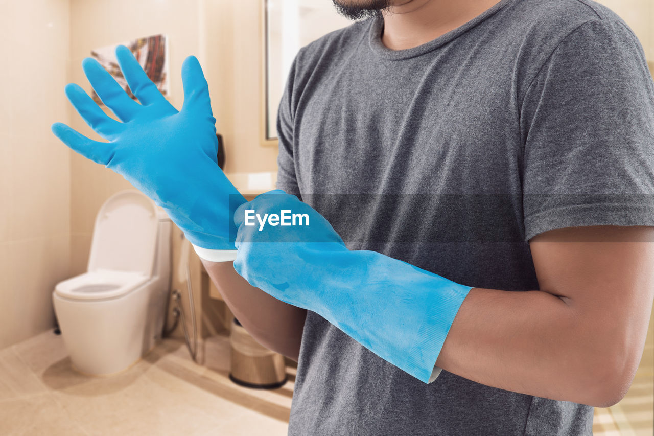 The man in a gray shirt wearing blue rubber gloves before washing the toilet.