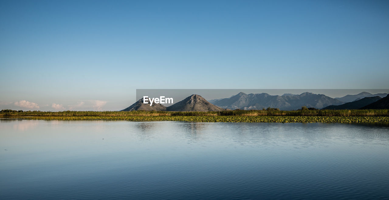 Scenic view of lake skadar by mountains against clear blue sky