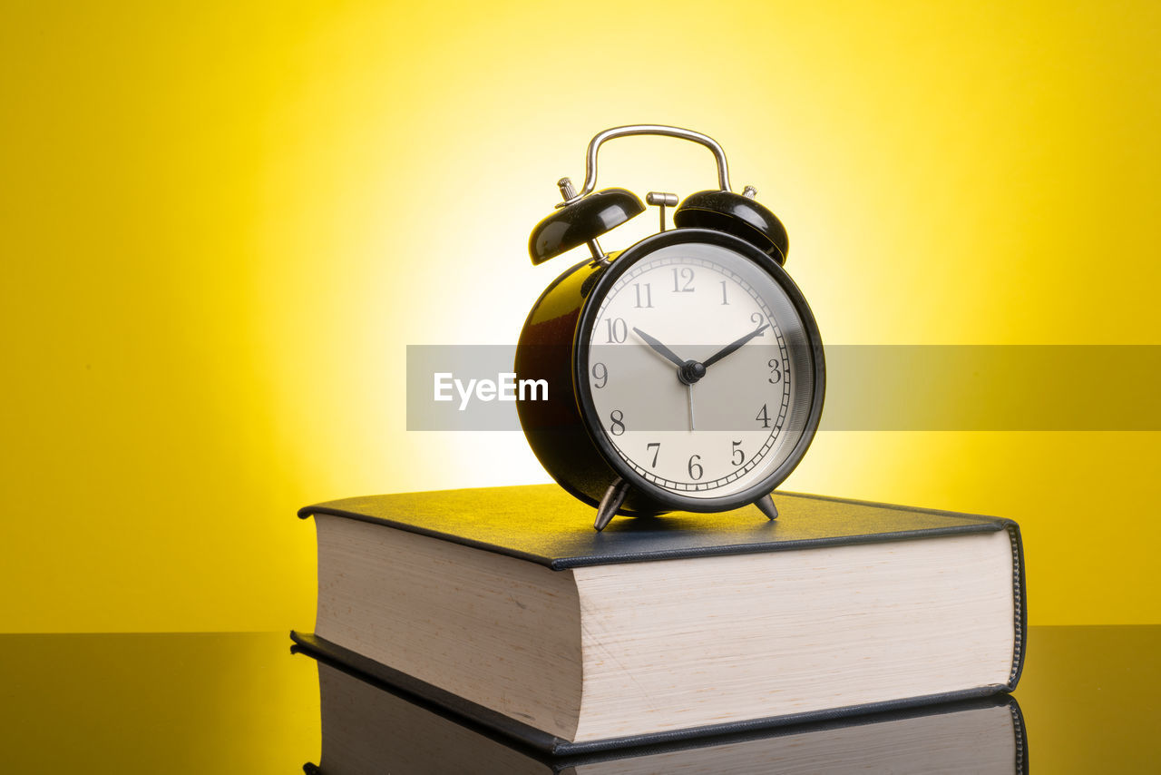 Alarm clock on book over table against yellow background